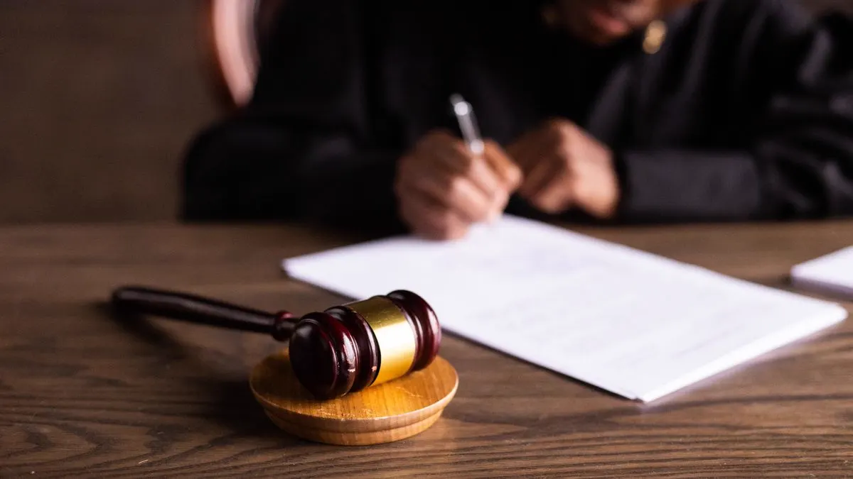 Eine Person in Richterrobe unterschreibt Dokumente, im Vordergrund ein Richterhammer