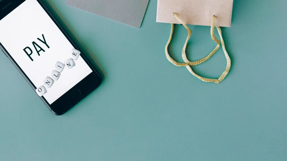 En mobiltelefon med texten Pay online bredvid en papperskasse