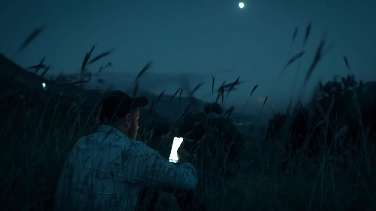 En ung man i mörkret, upplyst av skärmen på sin mobiltelefon